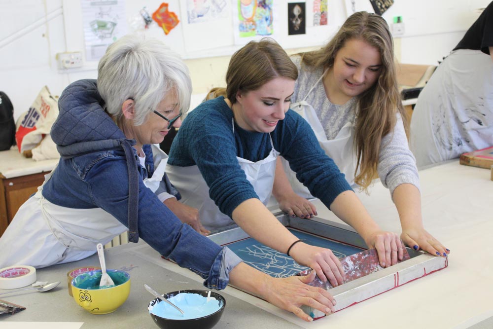 Two students and a teacher are screen printing.